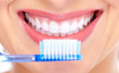 photo d'une jeune femme souriante montrant ses dents et tenant une brosse à dents bleue dans sa main droite