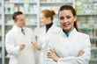 photo présentant une pharmacienne sans un premier plan et en arriere plan deux pharmacien en train de discuter devant le comptoir de médicaments