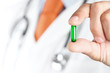 image représenatant la main d'un medecin tenant un comprimé sous forme de gellule et de couleur verte (couleur symbole santé)