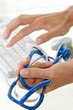 image des mains d'un médecin une sur le clavier et l'autre tenant un sthetoscope de couleur bleu